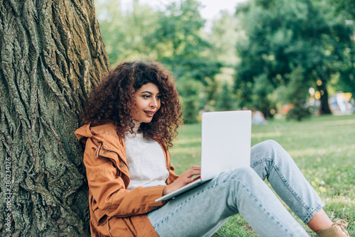 Selective focus of young freelancer using laptop neat tree in park