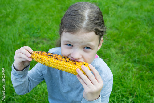 close-up  a girl  against the background of grass  eating corn cooked on the grill