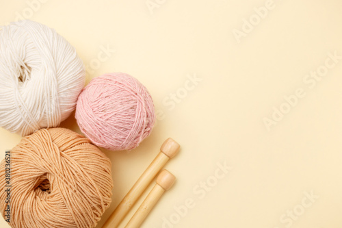 White and brown knitting wool and knitting needles on pastel background. Top view, flat lay, copy space
