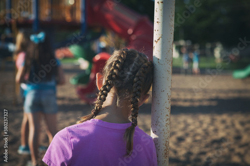 Recess: Lonely Girl Leans Against Swingset Watching Others