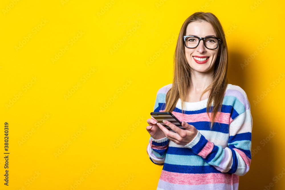 Young woman with a smile holds a phone on a yellow background. Banner Young woman with a smile holds a phone on a yellow background. Banner