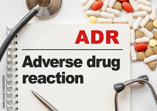 Page in notebook with ADR Adverse drug reaction on white background with stethoscope and group of pill. Medical concept. Term and abbreviation