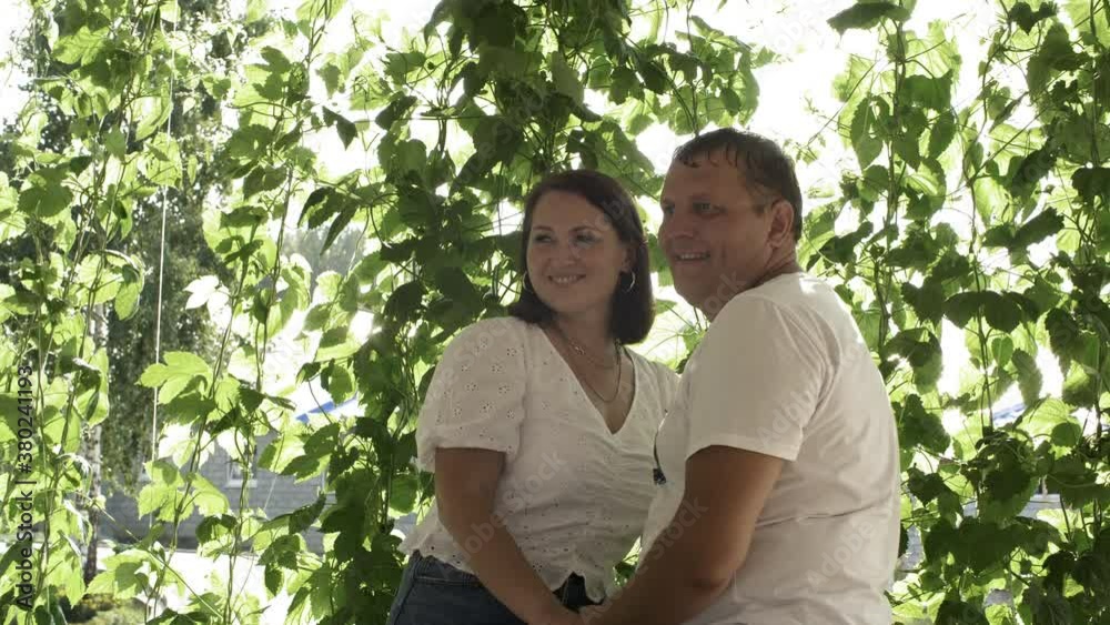 Beautiful happy middle aged couple standing and holding hands at summertime. Portrait of cheerful man and woman standing together near fresh green leaves at sunny summer day Beautiful happy middle aged couple standing and holding hands at summertime. Portrait of cheerful man and woman standing together near fresh green leaves at sunny summer day