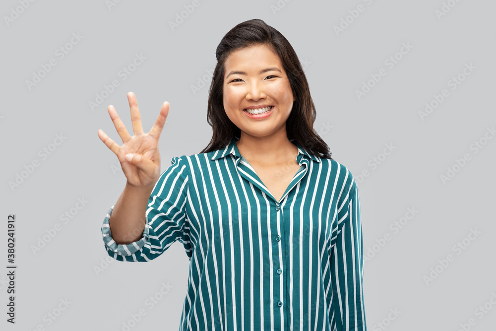 gesture, count and people concept - happy smiling asian woman showing four fingers over grey background gesture, count and people concept - happy smiling asian woman showing four fingers over grey background