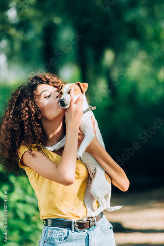 young woman in summer outfit kissing jack russell terrier dog in park