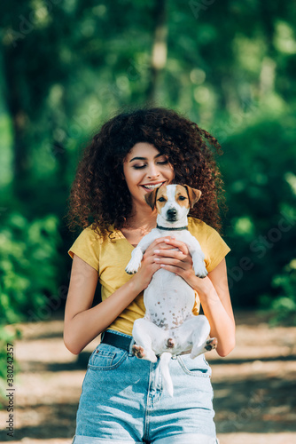joyful woman in summer outfit holding jack russell terrier dog in park