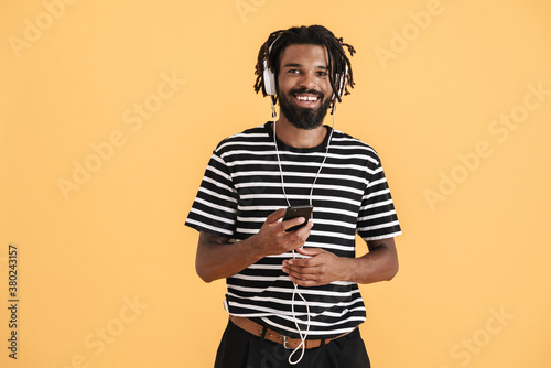 Photo of cheerful african american guy using cellphone and headphones