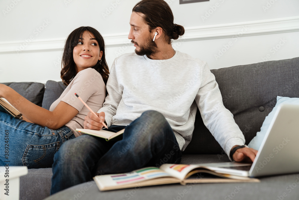 Image of pleased beautiful couple reading book and working with laptop Image of pleased beautiful couple reading book and working with laptop