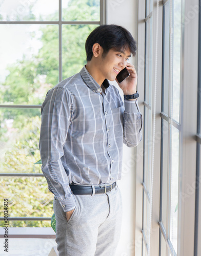 A young Asian businessman stands on the balcony of a window talking on the phone.