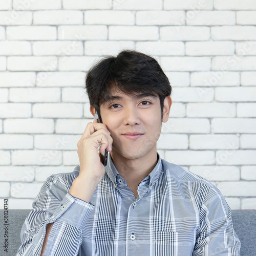 A young Asian man talking on his cell phone and smiling brightly.