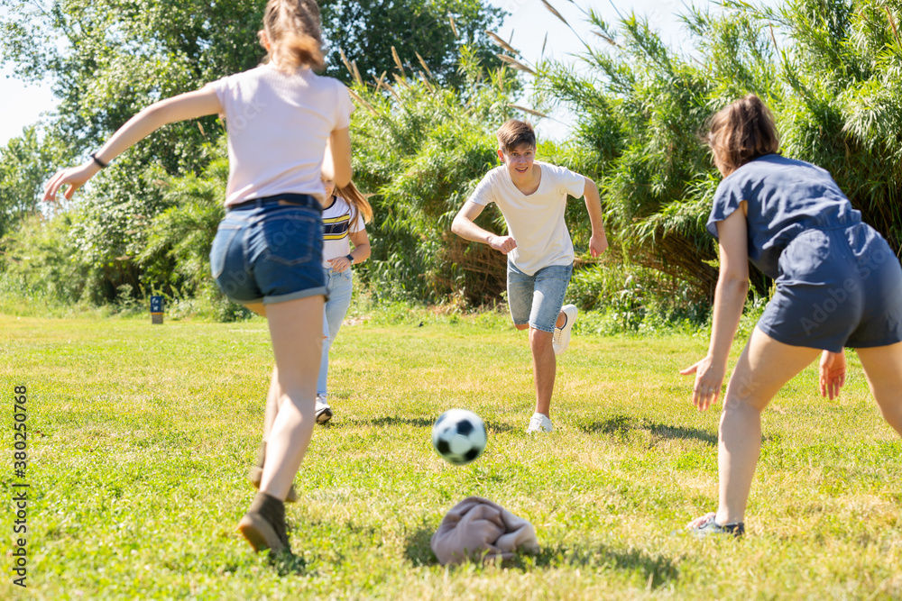 Obraz premium Company of glad teenagers playing football in park