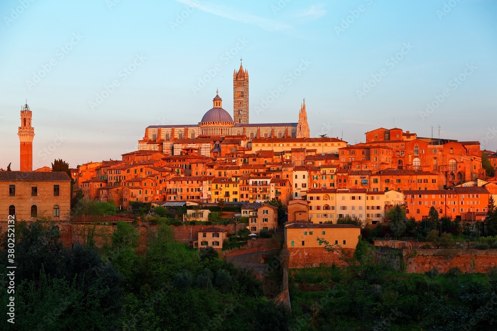 Sunset scenery of Siena, a beautiful medieval town on a hilltop in Tuscany Italy, with a view of architectural landmarks, Mangia Tower, Duomo Dome & Bell Tower bathed in warm, golden sunlight