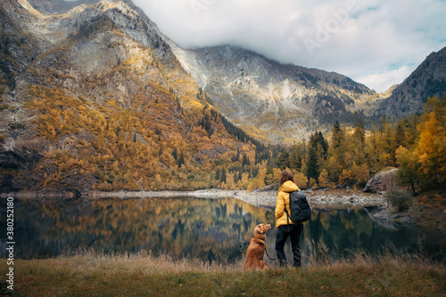 Traveling with the dog. A girl and a dog stand by a mountain lake in autumn. 