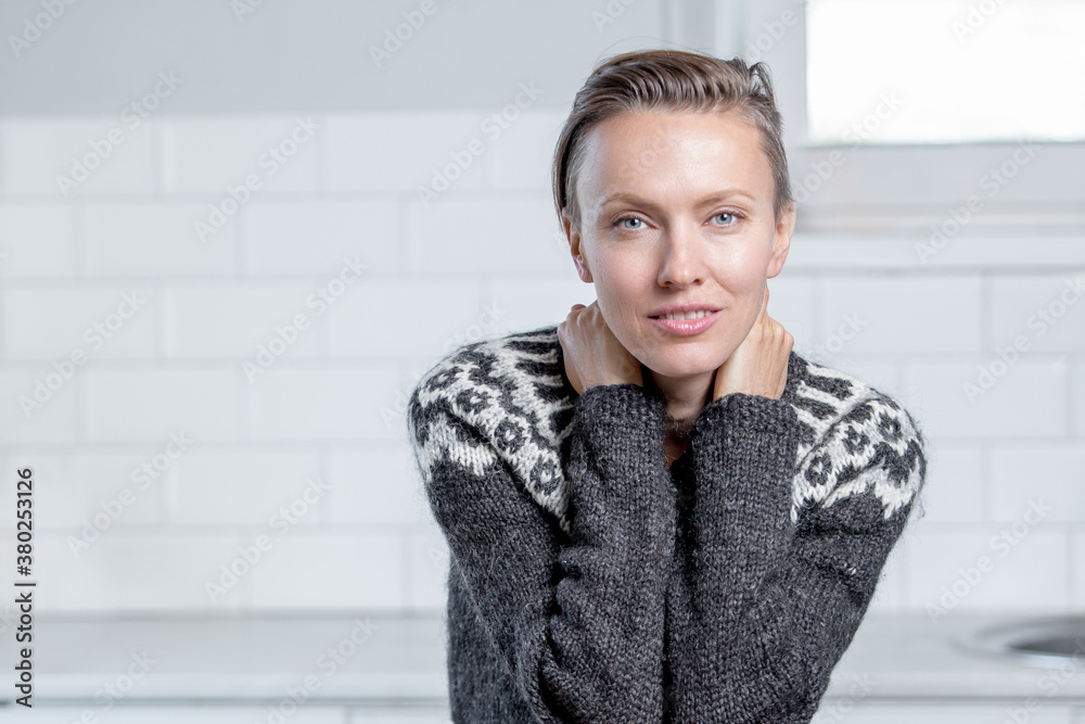Happy cheerful young woman with short hair, natural makeup over white kitchen background. Indoor portrait of beautiful brunette woman wearing knitted sweater smiling cheerfully Happy cheerful young woman with short hair, natural makeup over white kitchen background. Indoor portrait of beautiful brunette woman wearing knitted sweater smiling cheerfully