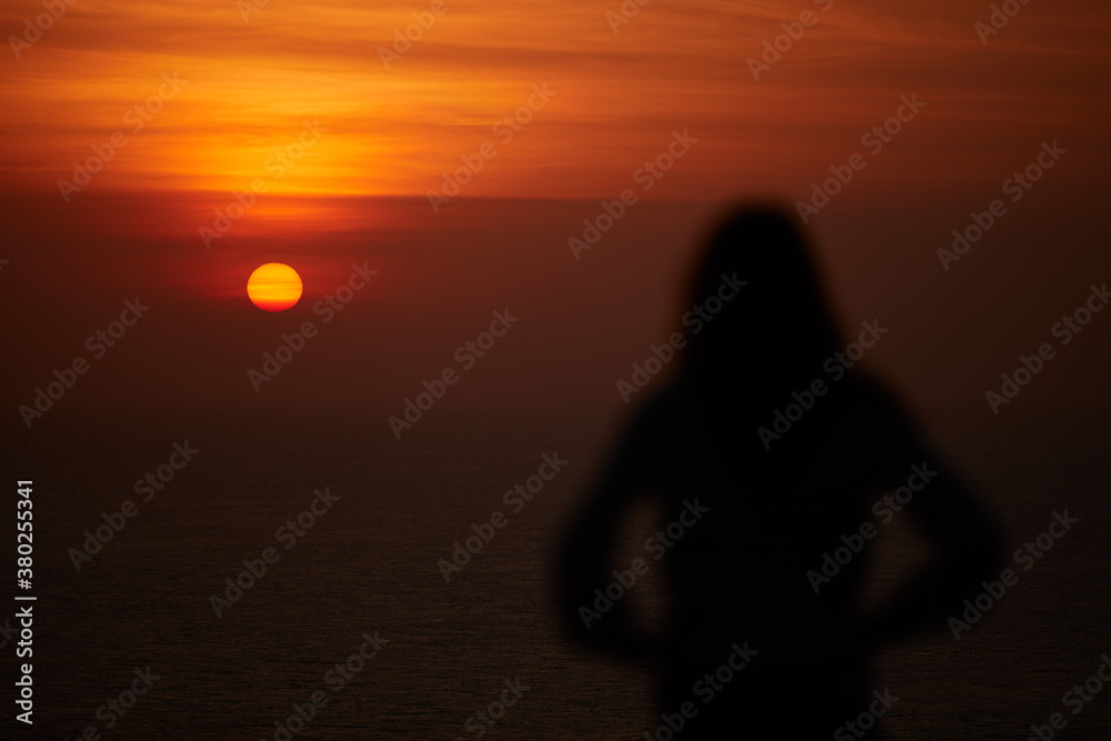 Silhouette of a woman with tropical sunset above the ocean.
