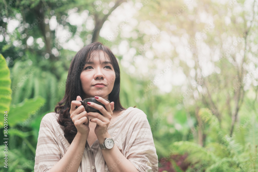 Young Asian woman relaxing at garden with a cup of coffee in a morning. A woman inhaled coffee Young Asian woman relaxing at garden with a cup of coffee in a morning. A woman inhaled coffee