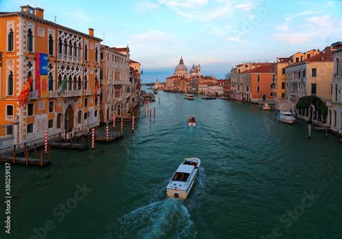 Romantic scenery of Venice at sunset, with boats, ferries & gondolas cruising on Grand Canal & the majestic landmark building Basilica di Santa Maria della Salute bathed in warm sunlight in background