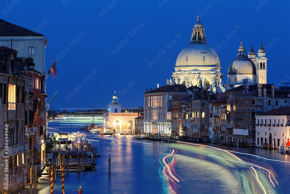Night scenery of romantic Venice in blue twilight, with light trails of ferries, boats & ships cruising on the Grand Canal and majestic Basilica di Santa Maria della Salute illuminated in background
