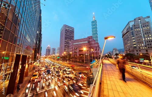 Evening view of a pedestrian footbridge over a busy street corner at rush hour & Taipei 101 Tower standing by World Trade Center in Xinyi Financial District ~A vibrant scene of Taipei Downtown at dusk