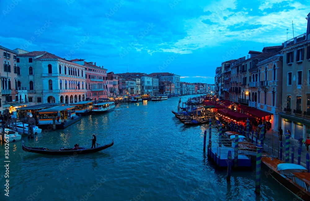 Scenery of Venice in blue dusk, with tourists riding in gondolas & water buses on Grand Canal and ferry boats parking by restaurants & bars, a view from Rialto Bridge (faded color, nostalgic effect)