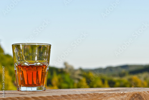 Glass with drink on a background of greenery and nature. Whiskey on an old wooden board. Sunny summer day. Mockup for design. Copy space and place for products. photo