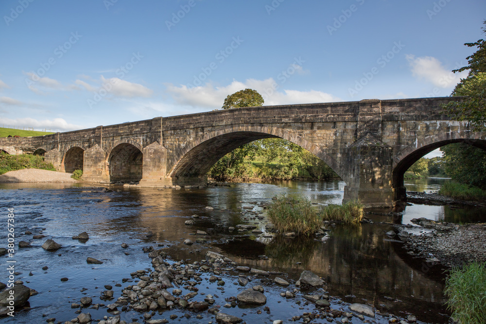 Large stone bridge crossing the river ribble near Clitheroe. Edisford bridge with rocks in the foreground 