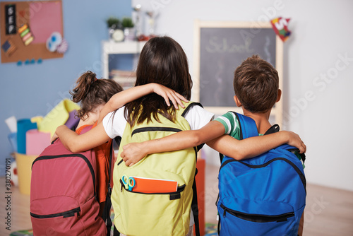 From behind. Three brothers embraced and carrying their backpacks