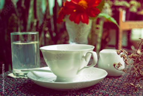 Vintage style photo Hot coffee in a beautiful white mug placed on a cute tablecloth on a beautifully arranged table in the morning.