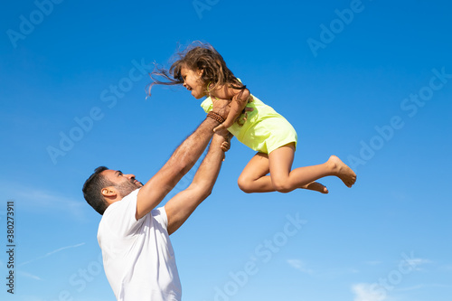 Joyful dad holding excited girl and throwing hands up in air. Handsome father and little daughter having fun outdoors, playing active games. Family outdoor activities concept
