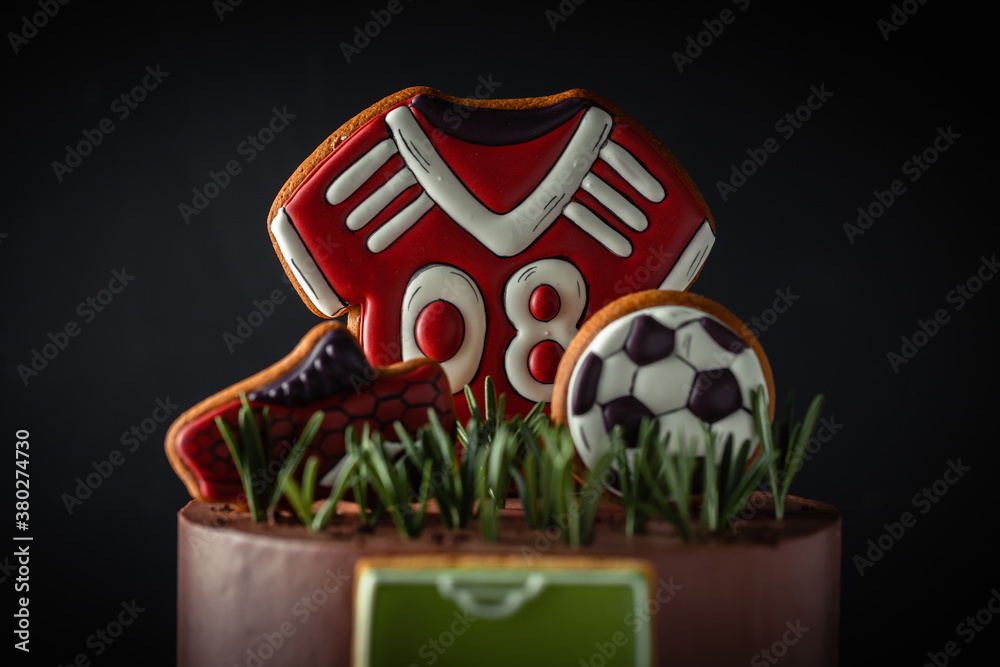 Birthday cake on the football theme on the black background. Gingerbread cookies in a shape of soccer ball, boot and T-shirt.