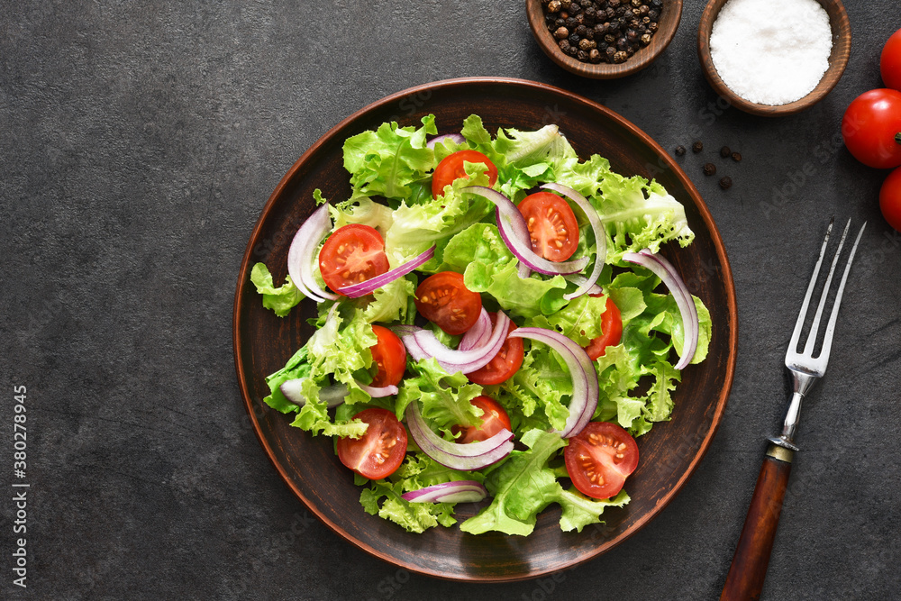 Vegetable salad with tomatoes, red onions and sauce on a black background.