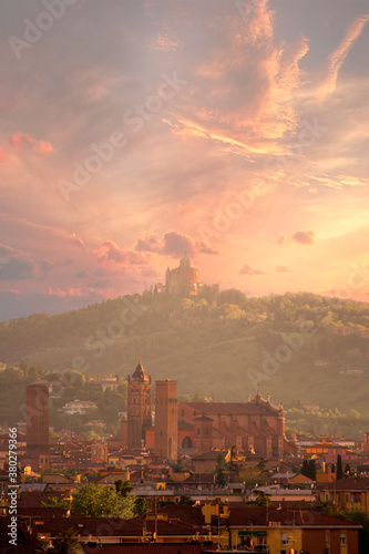 Aerial panoramic view of old Bologna city. It is saw Asinelli tower or torre  San Petronio church or basilica and San Luca church or basilica. Cloudy and sunset sky and bolognese hills in background