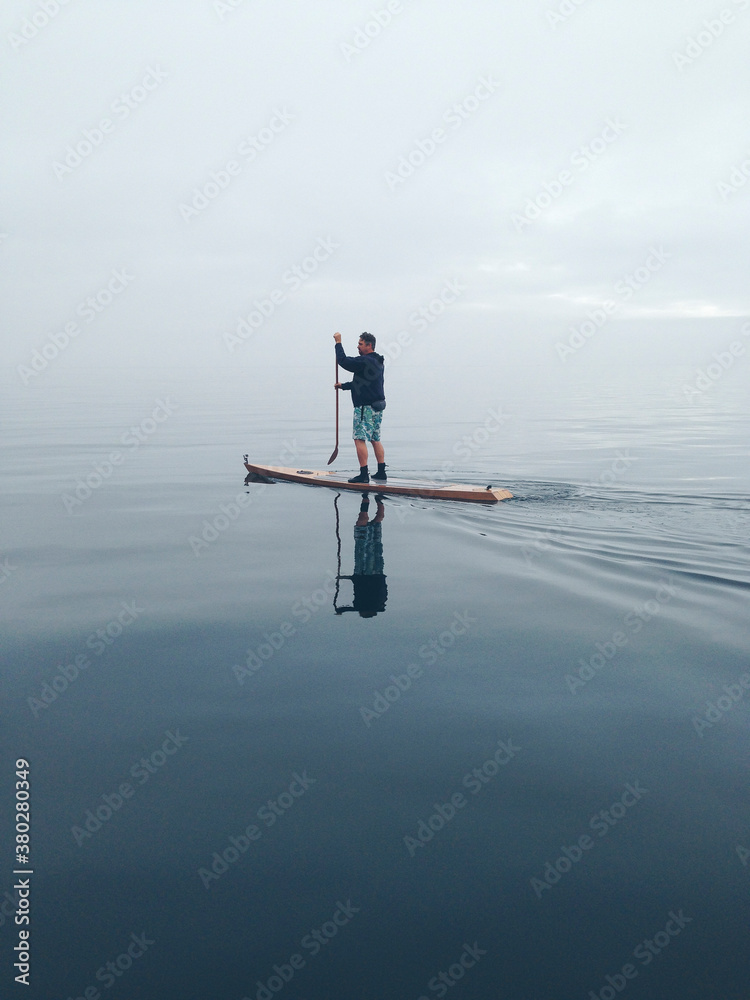 Man stand up paddling on calm, foggy waters Man stand up paddling on calm, foggy waters