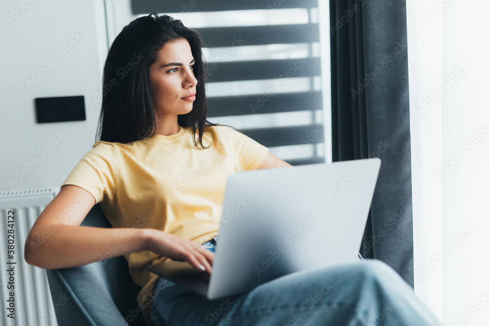 Young woman sitting on chair with laptop working at home Young woman sitting on chair with laptop working at home