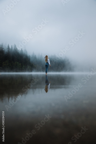Young caucasian girl standing in the foggy lake in the forest.