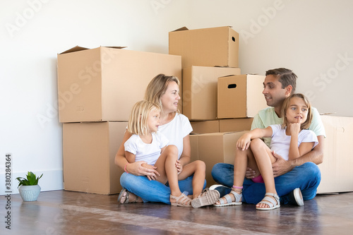 Happy Caucasian family sitting on floor with children. Mother, father and two daughters surrounded with cardboard boxes in new house or apartment. Mortgage, relocation and moving day concept © Mangostar