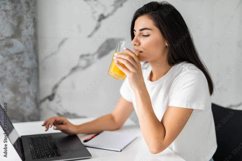 Attractive young woman using laptop and sitting in the kitchen Attractive young woman using laptop and sitting in the kitchen