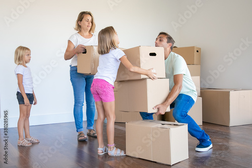 Young family carrying boxes into new home or apartment. Cute daughter helping father with belongings. Blonde mother in jeans standing and holding box. Mortgage, relocation and moving day concept © Mangostar