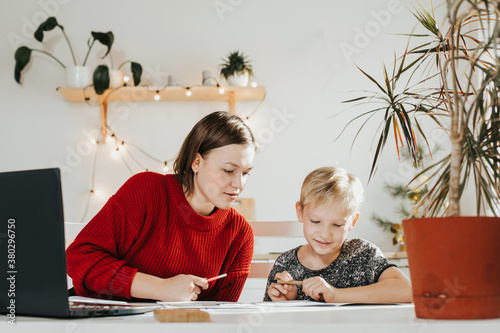Tutoring. Home schooling. Teacher and pupil. A woman and a blonde boy at the table.