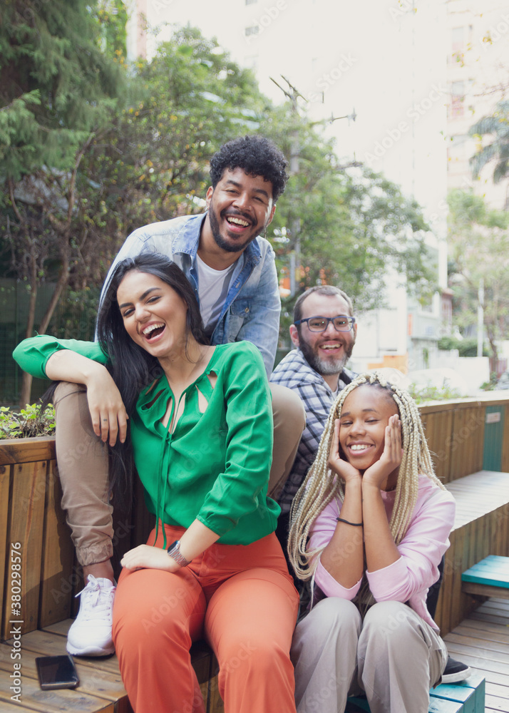 Happy multiracial friends sitting on bench talking and chilling at public area. Diversity and friendship