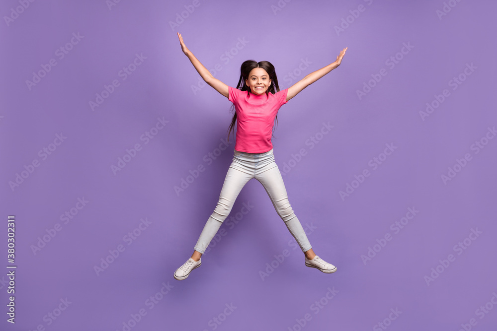 Full length body size photo of jumping high like a star happy cheerful schoolgirl wearing pink casual t-shirt jeans isolated on purple color background