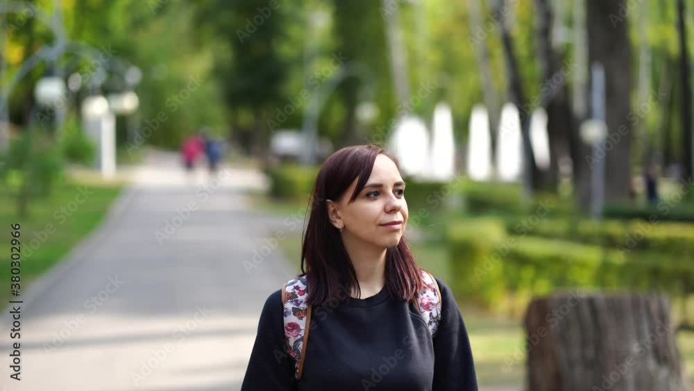 Pretty young woman with backpack walking in city park. Adult brunette strolling on street in sunny weather Pretty young woman with backpack walking in city park. Adult brunette strolling on street in sunny weather