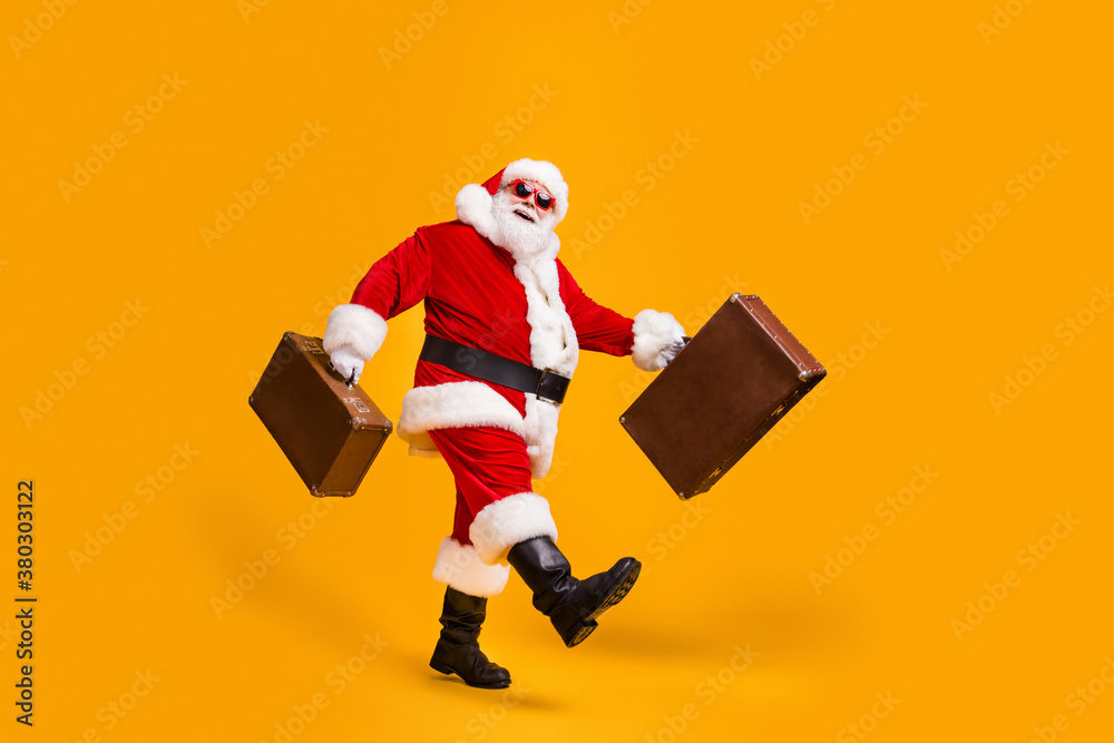 Full size profile side photo of white grey hair bearded santa claus go carry suitcase x-mas christmas eve travel wear headwear cap sunglass isolated bright shine color background Full size profile side photo of white grey hair bearded santa claus go carry suitcase x-mas christmas eve travel wear headwear cap sunglass isolated bright shine color background