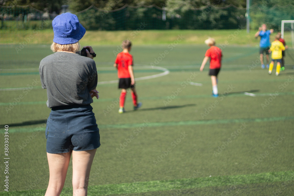 The girl takes pictures of sports. The girl is filming a football match. Girl in shorts on the playground. The girl takes pictures of sports. The girl is filming a football match. Girl in shorts on the playground.
