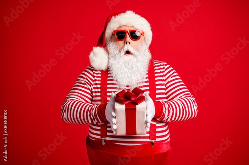 Portrait of his he nice handsome attractive amazed astonished Santa St Saint Nicholas holding in hands giftbox festal day December sale isolated bright vivid shine vibrant red color background © deagreez