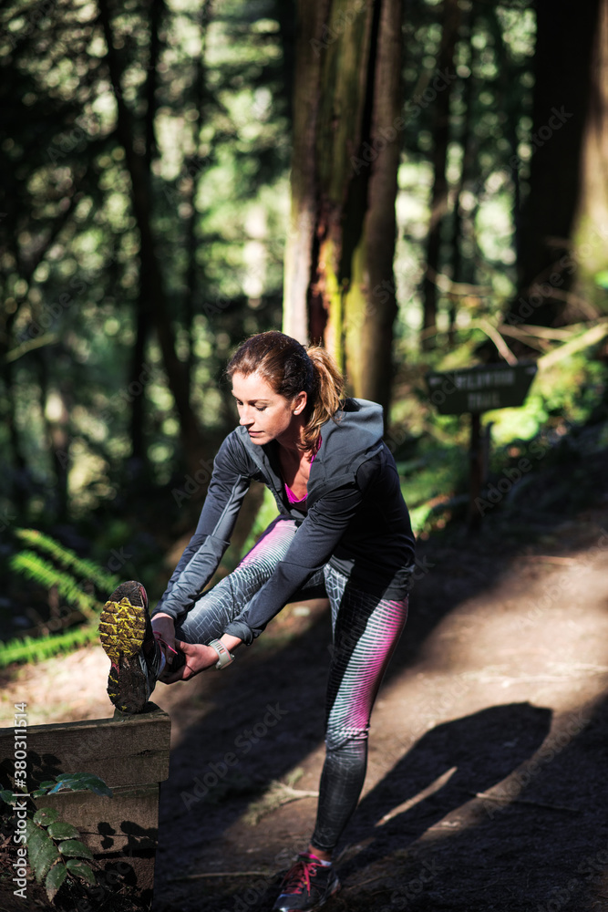 Woman in running clothes stretching in a sunspot on the trail. Woman in running clothes stretching in a sunspot on the trail.