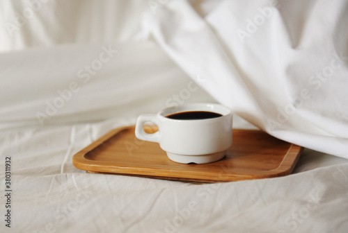 Morning awakening coffee in bed. White cup of black coffee on bamboo tray