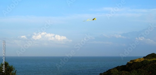 yellow kite against a blue sky with a few clouds above the sea