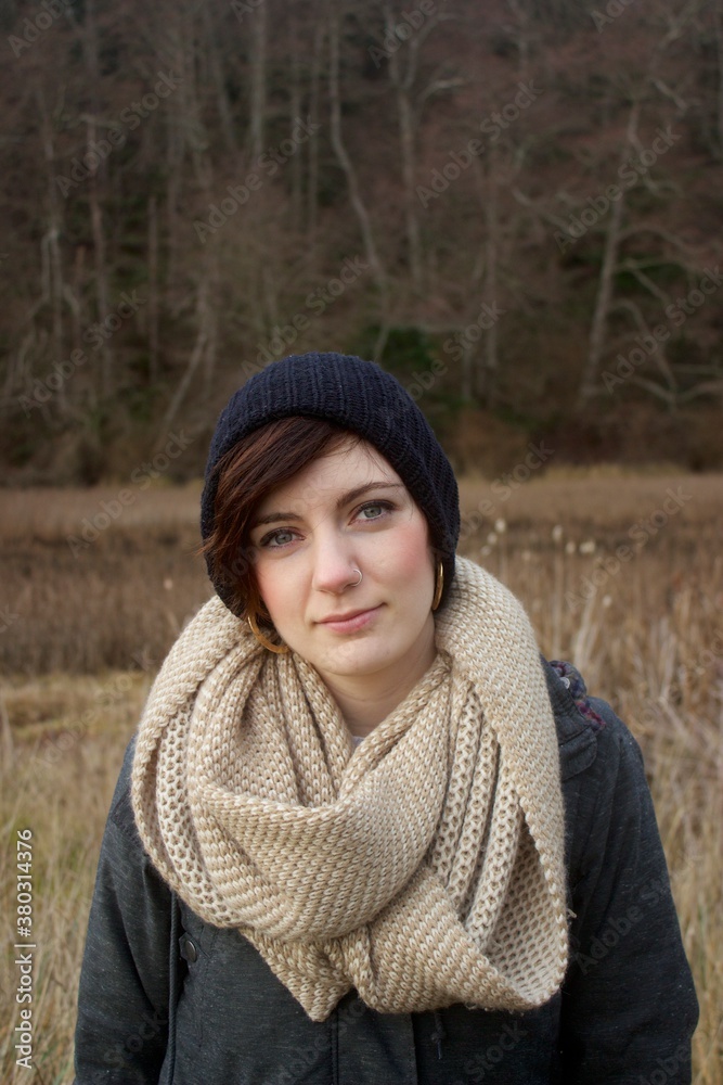 Young woman in coat and scarf looking at camera outdoors