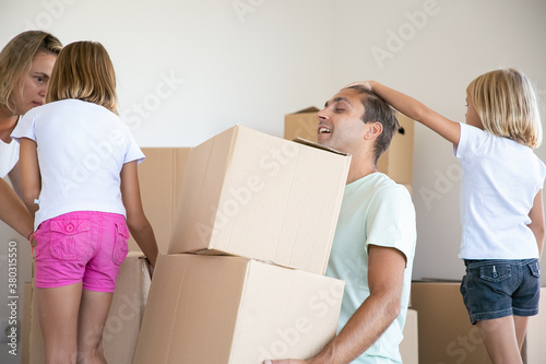 Middle-aged dad holding two carton boxes and sitting with closed eyes. Little girl touching father head. Mother talking with daughter. Family relocating. Mortgage, relocation and moving day concept © Mangostar